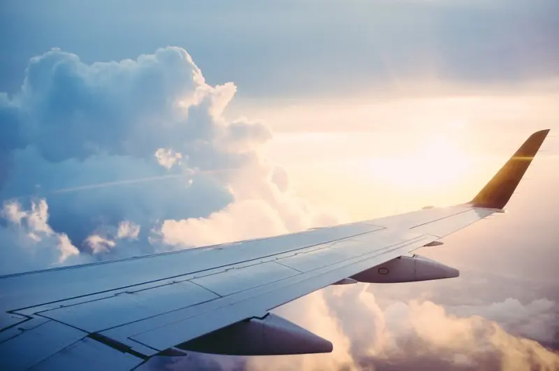 Aile d’avion au-dessus des nuages au coucher du soleil, symbolisant le départ à l’étranger et les avantages fiscaux du statut de non-résident.